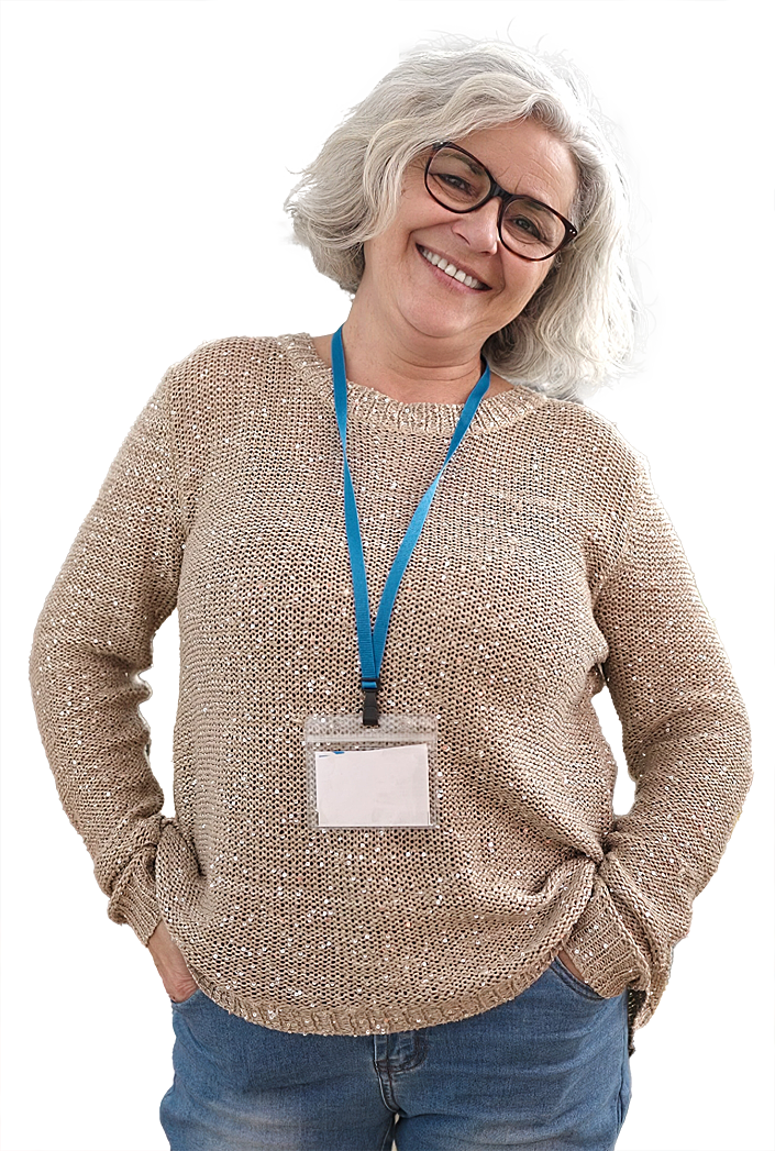 photo of a woman with grey hair and glasses, wearing an attendee badge. She is smiling casually, with her hands in her pockets.
