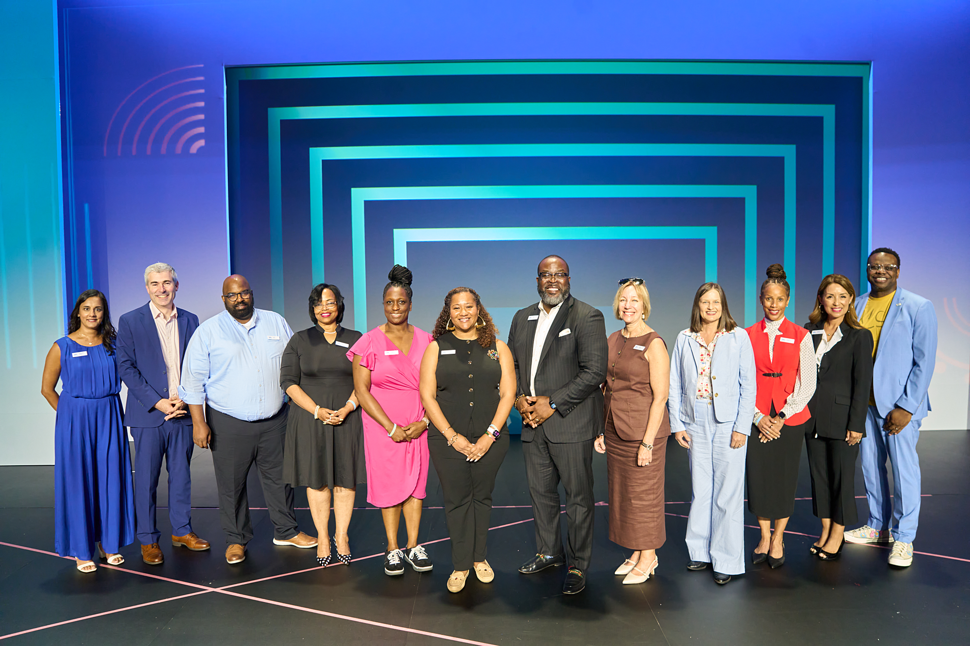 A photograph of a diverse group of adults standing on a stage against a colorful backdrop.