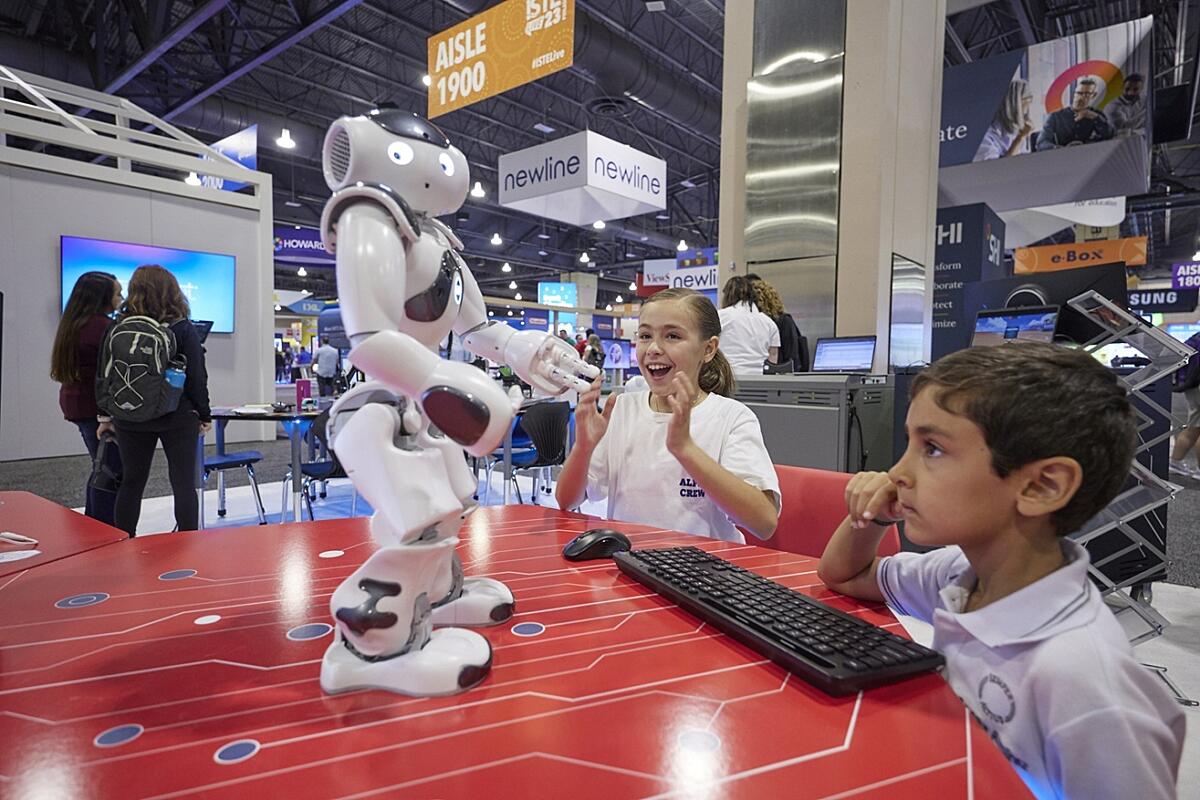Two students interacting with a small walking robot at a vendor display at an ISTE Live conference.
